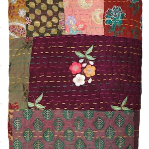 May include: A patchwork quilt with a variety of patterned fabrics in shades of brown, pink, and burgundy. The quilt features floral and leaf motifs, with embroidered details and colorful stitching. The overall design is a mix of textures and patterns.