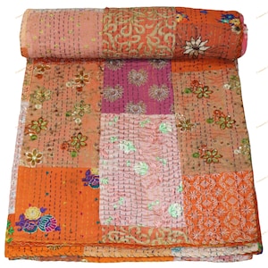 May include: A rolled-up, patchwork quilt featuring a variety of colors including orange, pink, and peach. The quilt is adorned with floral embroidery and decorative stitching. The design is a mix of geometric and floral patterns.