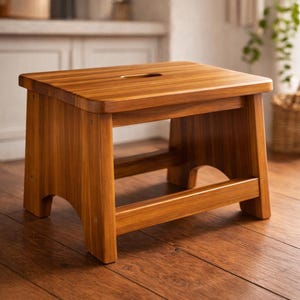 May include: A rectangular wooden step stool with a warm brown finish and visible wood grain. The stool features four sturdy legs, a horizontal support bar near the base, and a smooth top surface with a small, centered oval cutout handle.