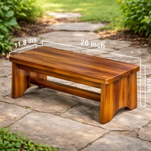 May include: A wooden bench in a warm brown hue, measuring 66 cm long and 30 cm wide. The bench features a rectangular top and solid legs, designed for outdoor spaces. The wood grain is visible.