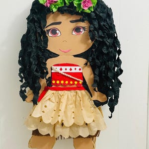 May include: A handmade pi&ntilde;ata in the shape of a cartoon character. The character has black paper hair, a red and white top, and a tan skirt. A green and pink floral crown sits atop the head. The pi&ntilde;ata is designed to resemble a popular animated character.