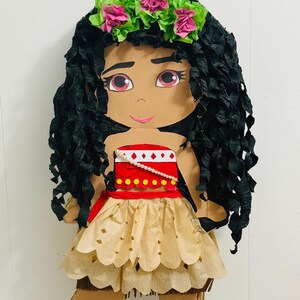 May include: A handmade pi&ntilde;ata in the shape of a cartoon character. The character has black paper hair, a floral crown, and a tan dress. The pi&ntilde;ata is designed with a red top and a tan skirt. The pi&ntilde;ata is designed to look like a cartoon character.