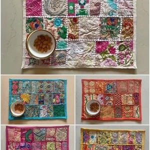 Könnte beinhalten: Eine Sammlung farbenfroher Patchwork-Tischsets mit aufwendigen Stickereien. Jedes Set zeigt eine einzigartige Kombination aus Mustern und Farben, darunter Rosa, Blau, Orange und Gelb. Auf jedem Set befindet sich eine kleine weiße Schale mit Goldrand, gefüllt mit Mandeln.