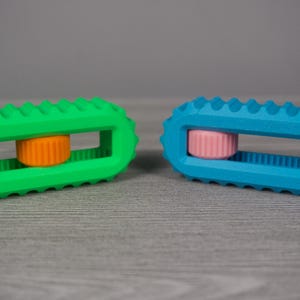May include: Two colorful, rectangular toys with a ridged design. One is bright green with an orange center, and the other is blue with a pink center. The toys have a textured, ridged exterior and a rectangular opening in the center.
