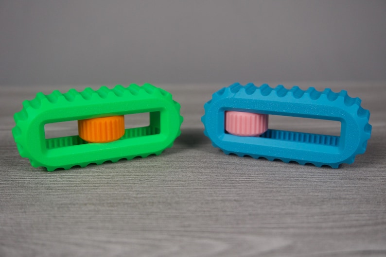 May include: Two colorful, rectangular toys with a ridged design. One is bright green with an orange center, and the other is blue with a pink center. The toys have a textured, ridged exterior and a rectangular opening in the center.