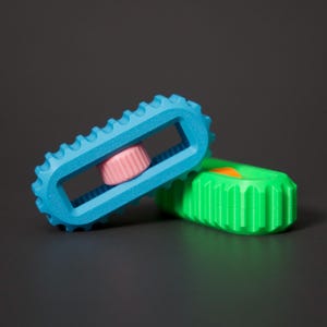 May include: Two colorful, geometric toys. One is light blue with a pink center and a ridged edge. The other is green with an orange accent. The toys are on a dark gray surface.