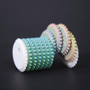 May include: A cylindrical object featuring a series of stacked, serrated-edge discs. The main body is a textured teal green with small, uniform spikes. The trailing discs transition in color from light blue to soft pink, yellow, and pale green.