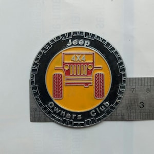 May include: Circular Jeep Owners Club emblem with a black border, yellow center, and red accents. The emblem features a Jeep 4x4 graphic and the words "Jeep" and "Owners Club". The emblem is approximately 3 inches in diameter.