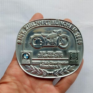 May include: Silver-colored motorcycle belt buckle with the text "8. Int. Zielfahrt München 1988." Features a motorcycle graphic and the text "R51 1938-1939 500 cm³ ohv 24 RS." Includes BMW and ADAC logos.