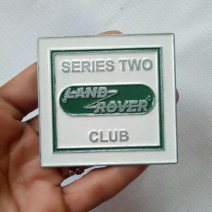 Puede incluir: Un emblema cuadrado blanco y verde del Land Rover Club. El emblema presenta las palabras "SERIES TWO" en la parte superior, el logotipo de Land Rover en el centro y "CLUB" en la parte inferior. El logotipo es verde con letras blancas.