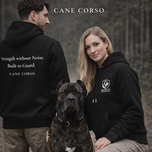 Puede incluir: Un perro Cane Corso con pelaje negro y marrón se encuentra entre dos personas que visten sudaderas negras. Las sudaderas tienen el texto "Strength without Noise. Built to Guard. CANE CORSO" en la espalda. La sudadera de la mujer tiene un logo que dice "SHADOW OF EMPIRE".