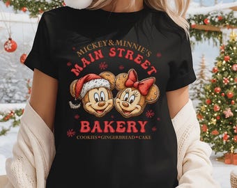 May include: Black t-shirt featuring Mickey and Minnie Mouse with the text "Mickey & Minnie's Main Street Bakery." Mickey is wearing a Santa hat, and Minnie has a red bow. The design includes snowflakes and the words "Cookies, Gingerbread, Cake."