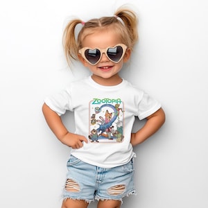 May include: A white t-shirt featuring the word "ZOOTOPIA" in green and a colorful graphic of characters from the movie. The shirt is worn by a young child wearing heart-shaped sunglasses and denim shorts.