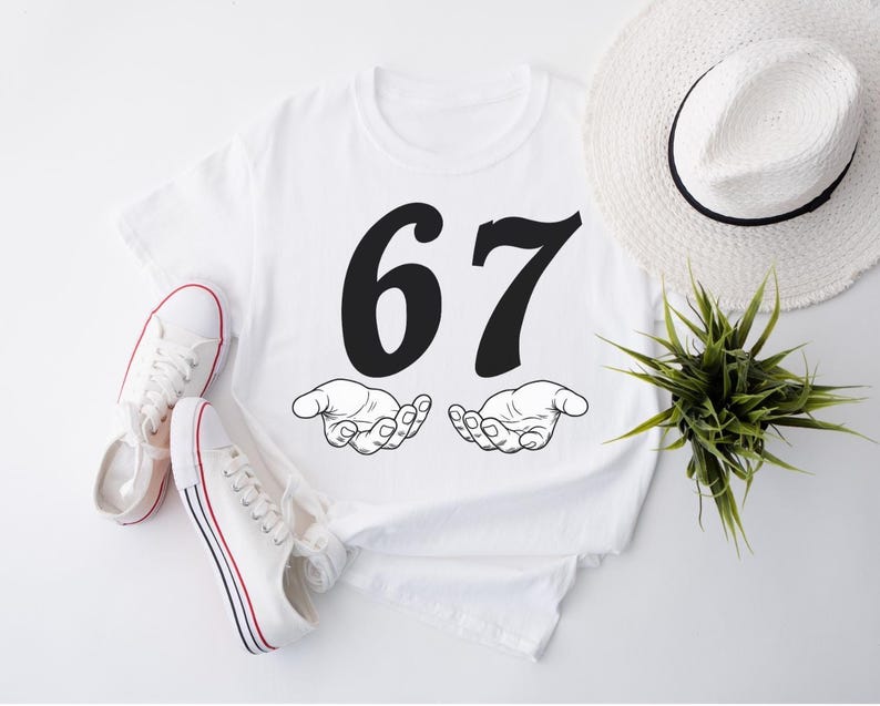 May include: White t-shirt with the number 67 in black, above two open hands. A pair of white canvas sneakers with red and blue stripes and a white hat with a black band are also in the image. A small green plant is also visible.