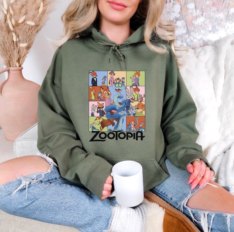 Pu&ograve; includere: Felpa con cappuccio verde oliva con una grafica colorata dei personaggi del film d'animazione "Zootropolis". La grafica &egrave; una griglia di immagini con il titolo del film in nero. La felpa ha un cappuccio con coulisse e una tasca a marsupio.