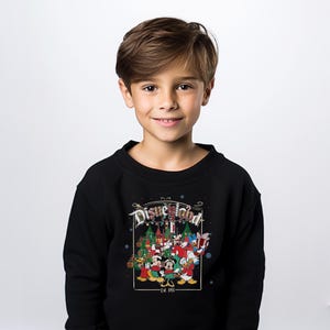 K&ouml;nnte beinhalten: Schwarzes Disneyland-Sweatshirt mit einem festlichen Motiv mit Mickey Mouse, Minnie Mouse, Donald Duck und anderen Disney-Figuren. Das Design umfasst Weihnachtsb&auml;ume und den Text "Disneyland - Est. 1955".
