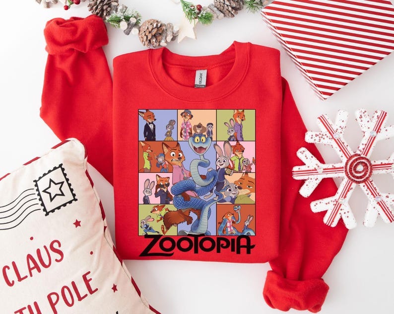 Pu&ograve; includere: Una felpa girocollo rossa con una grafica colorata dei personaggi del film "Zootropolis". La parola "Zootopia" &egrave; stampata in nero in basso. La felpa &egrave; circondata da decorazioni natalizie, tra cui un cuscino, una confezione regalo e un ornamento a forma di fiocco di neve.