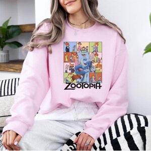 Pu&ograve; includere: Una felpa rosa chiaro con una grafica colorata del film d'animazione "Zootropolis". La grafica &egrave; una griglia di personaggi con il titolo del film in nero. La felpa ha maniche lunghe e girocollo.