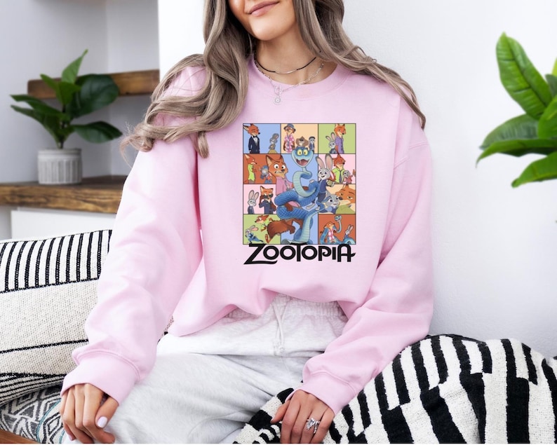 Pu&ograve; includere: Una felpa rosa chiaro con una grafica colorata del film d'animazione "Zootropolis". La grafica &egrave; una griglia di personaggi con il titolo del film in nero. La felpa ha maniche lunghe e girocollo.
