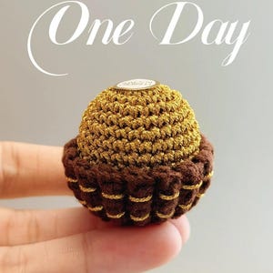 Puede incluir: Una magdalena de ganchillo con la parte superior dorada y la base marrón, acentuada con hilo dorado. La imagen incluye el texto "One Day" y la frase "Life should be beautiful and gentle. I hope you are too."