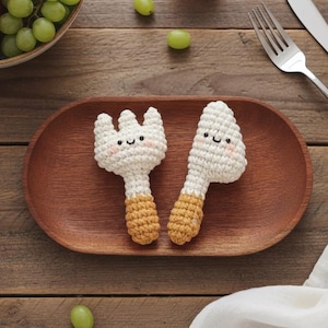 Puede incluir: Una bandeja de madera contiene un juego de tenedor y cuchillo de ganchillo con caras sonrientes y mangos de color canela. Un cuenco de fruta y un tenedor y cuchillo de acero inoxidable también están en la imagen.