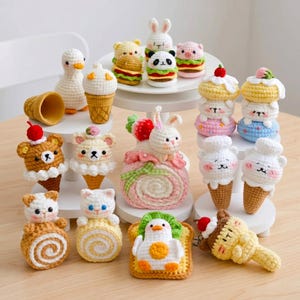 Op de afbeelding: Een verzameling kleine, handgemaakte gehaakte amigurumi-figuurtjes in de vorm van dieren en etenswaren. De set bevat diverse personages zoals een witte eend, een panda, een varken en beren, geïntegreerd met ijshoorntjes, taartjes en toast.