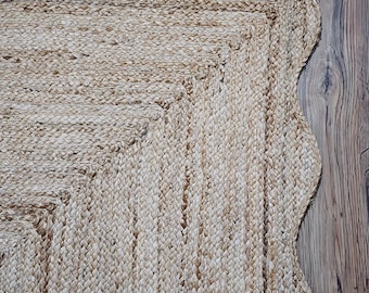 Könnte beinhalten: Ein natürlicher Jute-Teppich mit gewelltem Rand. Der Teppich hat eine rechteckige Mitte mit einem gewebten Muster und einer hellbraunen Farbe. Der Teppich liegt auf einem Holzboden.