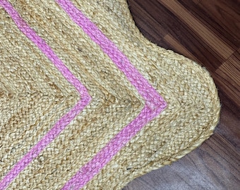 May include: A natural jute rug with a scalloped edge. The rug features three vibrant pink stripes running diagonally across the surface. The rug's neutral color and playful design make it a versatile home decor item.