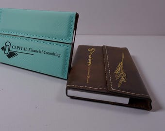 May include: A light blue business card holder with the text CAPITAL Financial Consulting and a paperclip icon, and a brown business card holder with the text Penelope Wedding Planner and a gold botanical illustration, both featuring visible stitching.