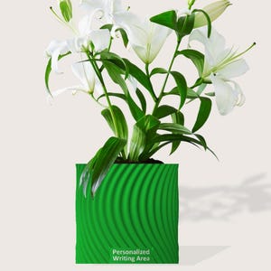May include: A vibrant green square planter with a textured, wave-like design, holding a lush arrangement of white lilies and green foliage. The planter has the text "Personalized Writing Area" on the front.