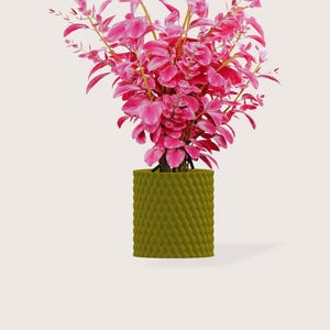 Op de afbeelding: Een arrangement van helder roze kunstbloemen met delicate bladeren en stelen, gepresenteerd in een getextureerde, olijfgroene cilindrische pot. De plant voegt kleur en een vleugje natuur toe aan elke ruimte.