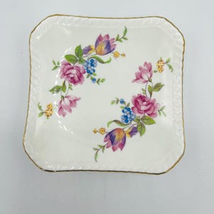 May include: A square, off-white porcelain dish with a gold rim and floral design. The flowers are pink, purple, yellow, and blue. The dish has a scalloped edge.