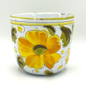 May include: A white ceramic planter with a hand-painted floral design. The planter features a large yellow flower with green and brown leaves. A yellow and green border accents the rim. The planter is approximately 4 inches in diameter.