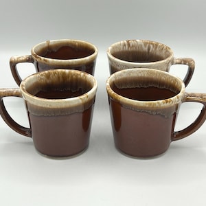 May include: Four brown ceramic mugs with a cream-colored rim and handle. The mugs have a glossy finish and a classic, simple design. The mugs are empty and ready to be filled with coffee or tea.