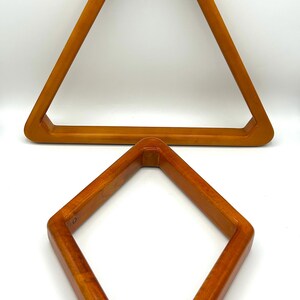 May include: Two wooden billiard ball racks. One is a triangle shape, and the other is a diamond shape. Both are made of a light brown wood with rounded edges. The triangle rack is larger than the diamond rack.