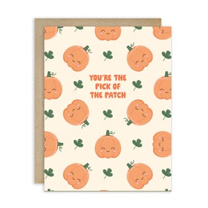 May include: Greeting card with a beige background featuring a pattern of smiling orange pumpkins and green clovers. The text "YOU'RE THE PICK OF THE PATCH" is in orange. The card is set against a brown envelope.
