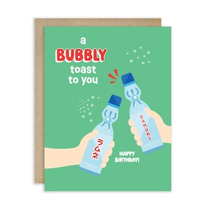 May include: Greeting card with a green background and a bubbly toast message. Two hands are holding up Ramune soda bottles. The card says "Happy Birthday!"
