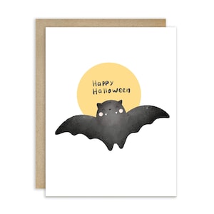 May include: A Halloween greeting card featuring a cartoon bat with a smiling face, set against a yellow circle resembling a moon. The words "Happy Halloween" are written above the bat in black text. The card has a white front and a brown border.