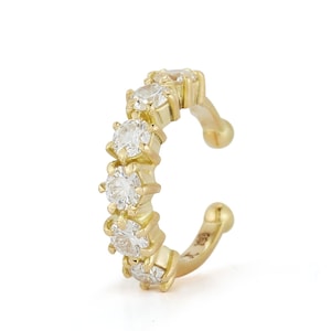 Può includere: Un ear cuff in oro con cinque pietre rotonde e trasparenti, incastonate a griffe e disposte in una fila verticale lungo la curva esterna. La fascia in metallo lucido termina con estremità arrotondate, progettata per aderire senza fori.