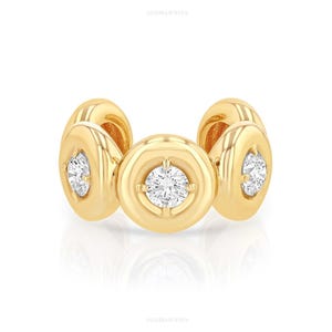 May include: A gold ear cuff featuring three circular, polished gold settings, each containing a single, round, brilliant-cut white diamond. The design consists of a central circular element flanked by two smaller, matching circular side elements.