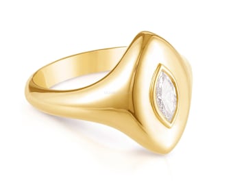 May include: A polished yellow gold ring featuring a smooth, tapered band that widens into a pointed, shield-like face. Centered on the face is a single, clear, marquise-cut gemstone set vertically, creating a sleek and reflective metallic surface.