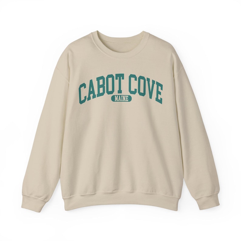 May include: A beige sweatshirt with a teal blue arch design that reads "CABOT COVE MAINE".