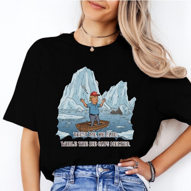 May include: Black t-shirt featuring a cartoon illustration of a man in a boat amidst melting icebergs. The text reads "Trust me, he said, while the ice caps melted."