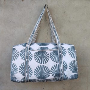 May include: A white and blue seashell-patterned tote bag with two handles. The bag is rectangular with a zipper closure and a repeating pattern of blue seashells. The handles and trim are a matching blue and white striped design.