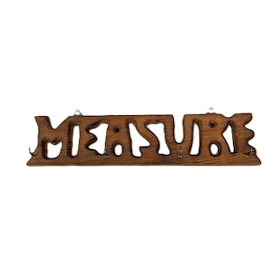 May include: A wooden sign with the word "MEASURE" cut out in a rustic font. The sign is brown and has small hooks underneath. It is designed to be hung on a wall.