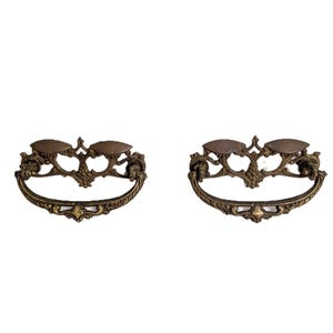 May include: A pair of matching antique-style brass drawer pulls featuring ornate, scrollwork backplates with two mounting points each and curved, swinging bail handles with detailed relief patterns across the metal surface.