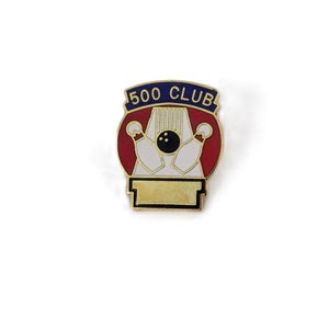 May include: Gold-colored bowling pin 500 Club pin with a red, white, and blue design. The pin is on a gold-colored base with the text "500 CLUB" on a blue banner.