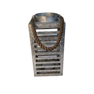 May include: A rectangular metal lantern with a rope handle. The lantern has a galvanized finish and horizontal slats. The rope handle is thick and brown. The lantern is designed to hold a candle or other light source.