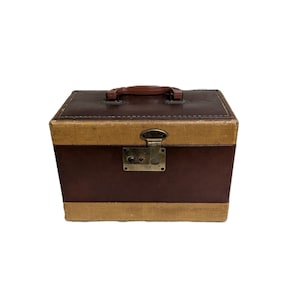 May include: A rectangular storage case featuring alternating horizontal bands of dark brown and tan textured material. The case includes a brown plastic top handle, a central metal latch mechanism, and a keyhole plate on the front face.