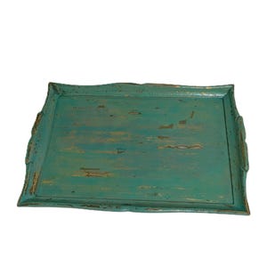 May include: A rectangular serving tray with a distressed teal finish, featuring raised edges and integrated side handles. The surface shows visible wear with patches of brown wood grain showing through the chipped turquoise paint.